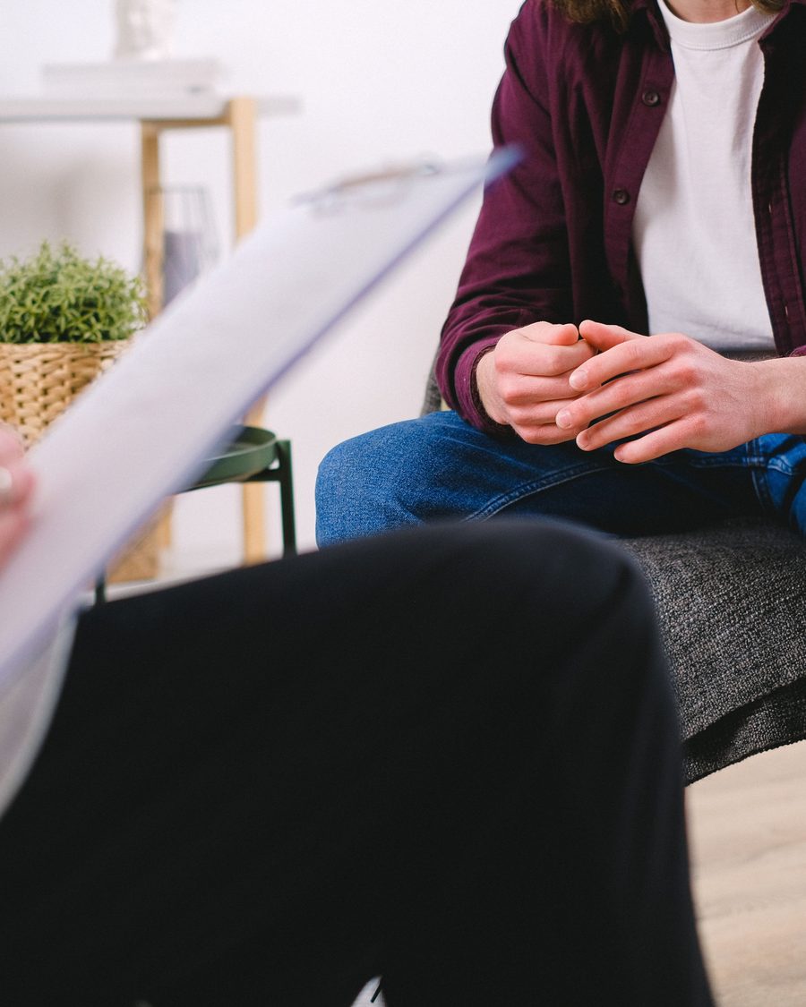 A person sitting quietly in a counselling session, hands clasped, a glass of water on the table beside them.